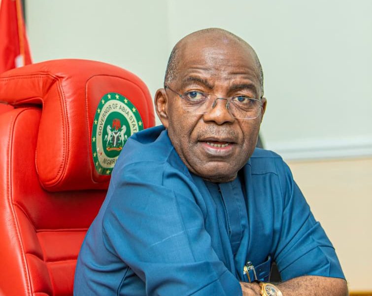 Governor Alex Otti seating on the Governor's seat with folded arms on the table, looking at camera